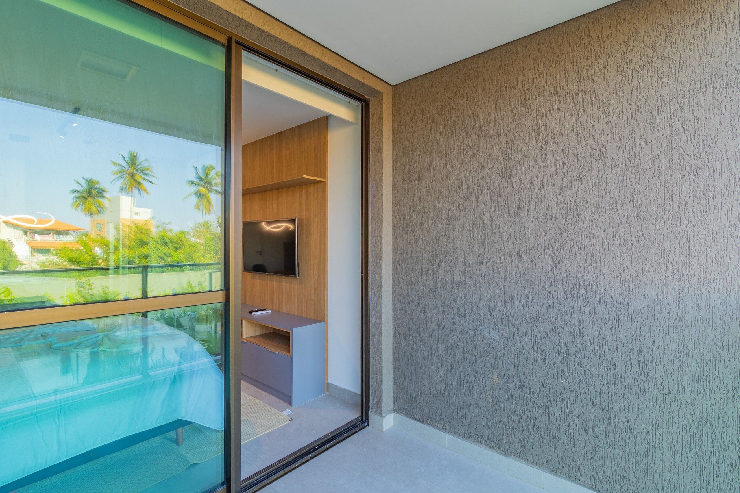 Una habitación moderna con balcón de vidrio, televisión de pantalla plana y estante de madera.