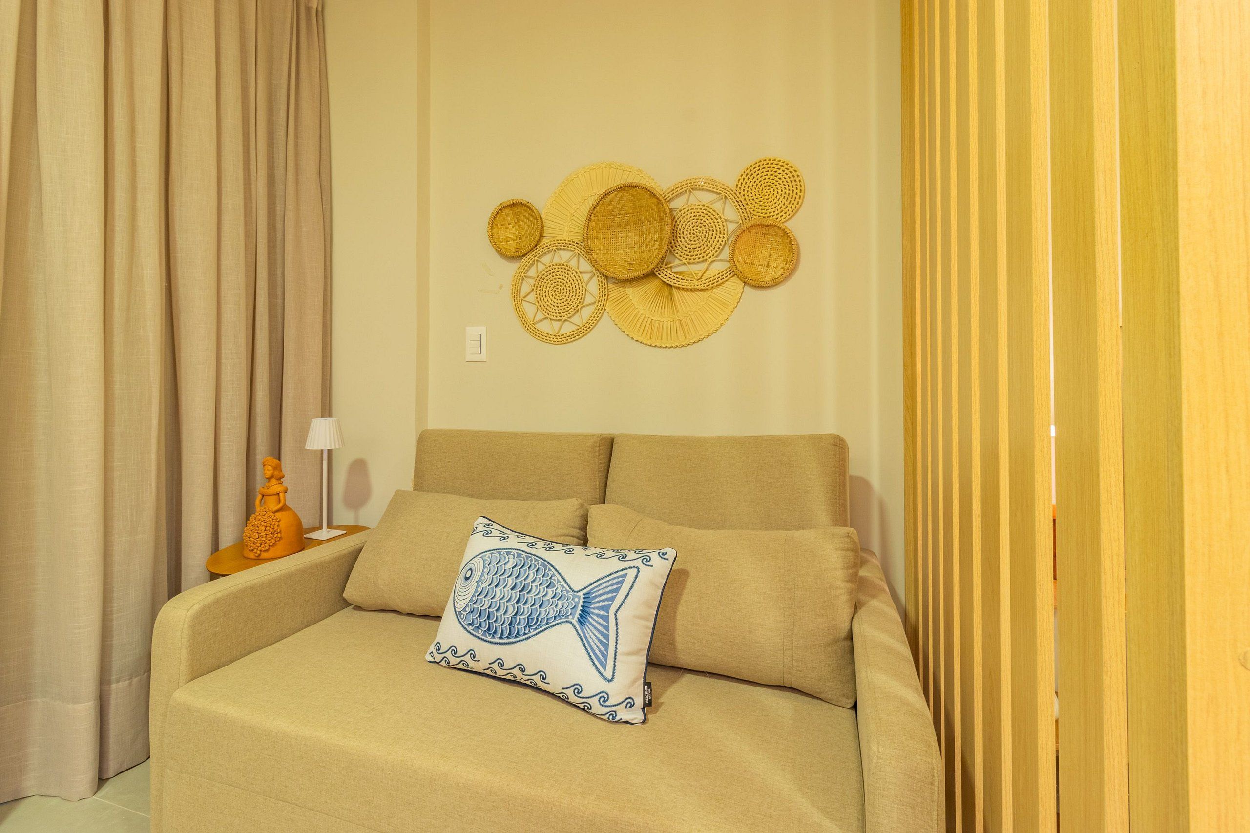 En beige sofa med en pude med fiskemønster, en billedkunst og en træafskærmning.