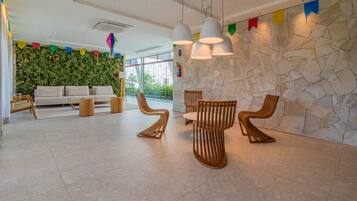 Un vestíbulo moderno con pared de piedra, pared verde con plantas, un sofá, sillas de madera y lámparas colgantes.