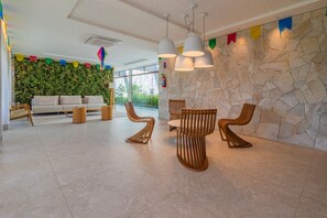 A modern lobby with a stone wall, a green wall with plants, a sofa, wooden chairs, and hanging lights. - Beach Class Summer by Carpediem (Ipojuca)