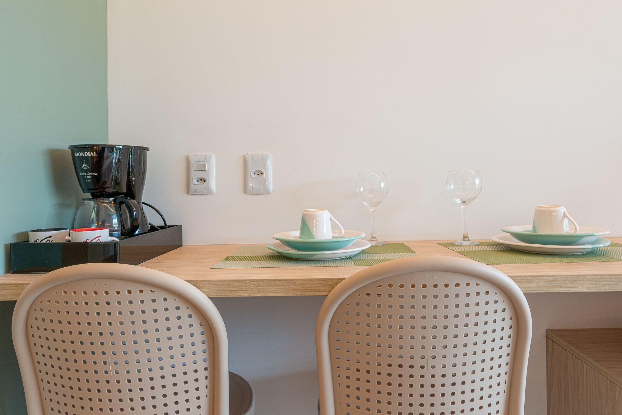 A dining area with a wooden table, two chairs, a coffee maker, and two wine glasses.
