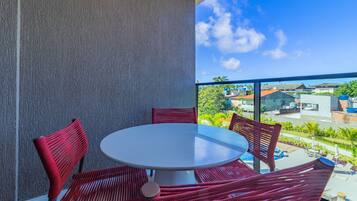 Un balcón con una mesa redonda y sillas de mimbre rojas, con vistas a una zona residencial con casas y vegetación.