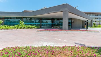 Un edificio moderno con techo curvo, grandes ventanales y un área de entrada pavimentada con macizos de flores.