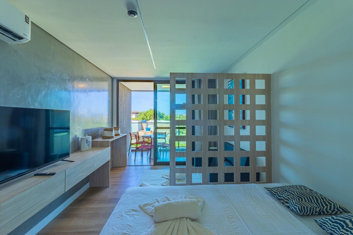 Ein modernes Hotelzimmer mit einem großen Flachbildfernseher, einem Bett mit weißer Bettwäsche, einer Holzwand und einem Balkon mit Sitzgelegenheit.