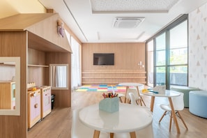Una sala giochi per bambini in stile moderno, con mobili contenitori in legno, televisore e un'ampia finestra.