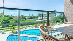 A balcony with a view of a swimming pool, lounge chairs, and a building in the background. - Beach Class Summer by Carpediem (Ipojuca)