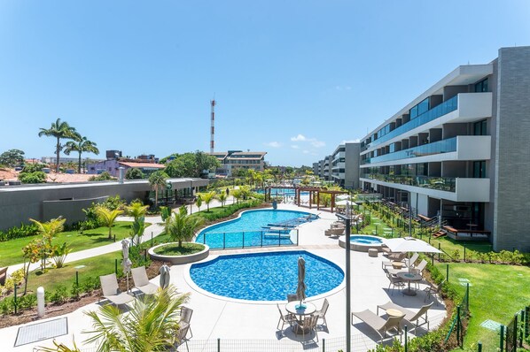 Un resort con una grande piscina centrale, aree salotto all'aperto e un edificio moderno con balconi.