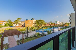Un área de piscina con sillones de descanso y sombrillas, rodeada de vegetación y edificios.