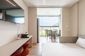 Une chambre d’hôtel comprenant un lit, un bureau avec une machine à café, une télévision et un balcon avec des chaises.
