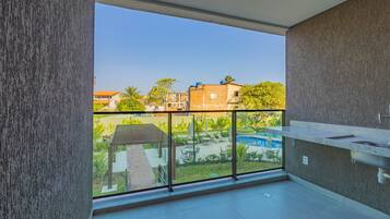 A balcony with a view of a swimming pool and greenery, a modern kitchen area, and a tiled floor.