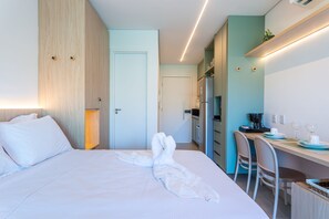 A hotel room with a bed, a desk, a chair, a kitchenette, and a bathroom door. - Beach Class Summer by Carpediem (Ipojuca)