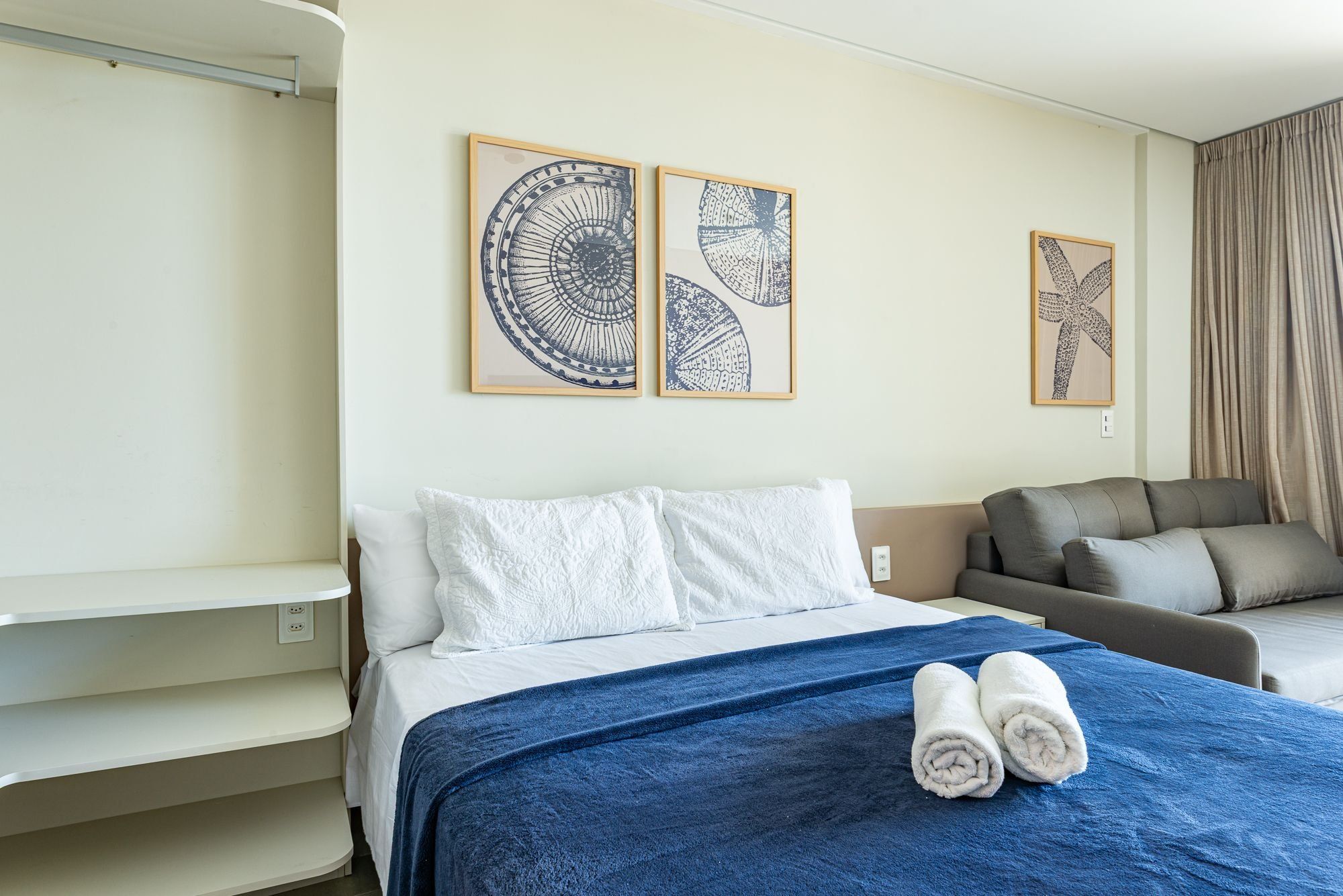 A hotel room with a bed, a sofa, and two framed wall art pieces.
