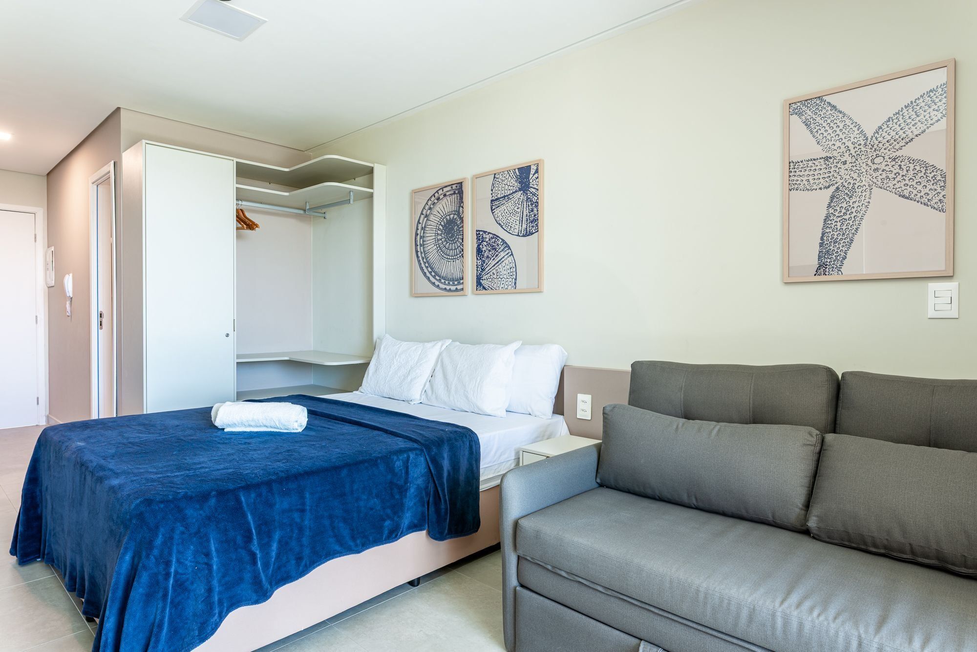 Quarto com cama, sofá cinzento e duas obras de arte nas paredes.