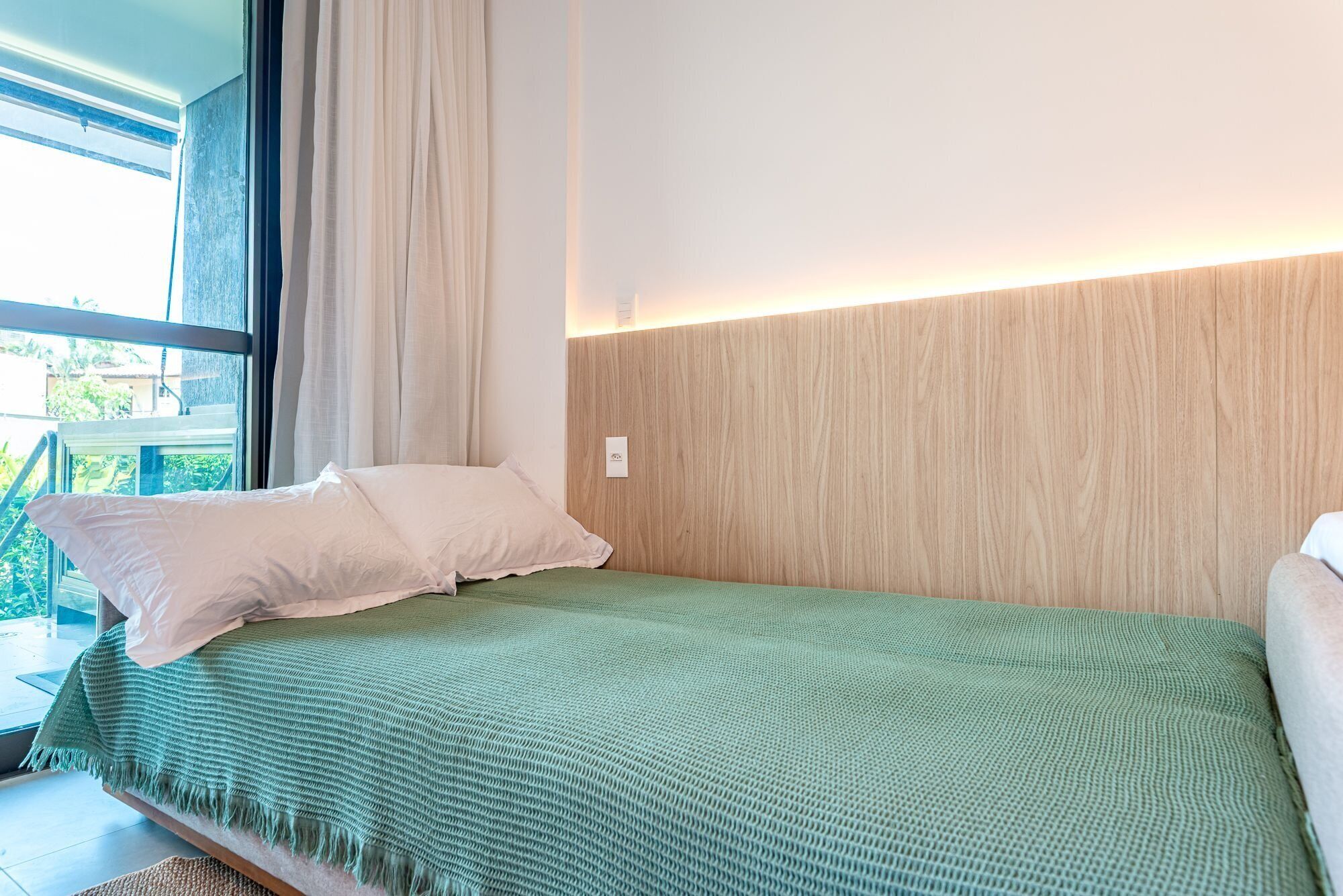 Una cama individual con una manta verde, almohadas blancas y un cabecero de madera.