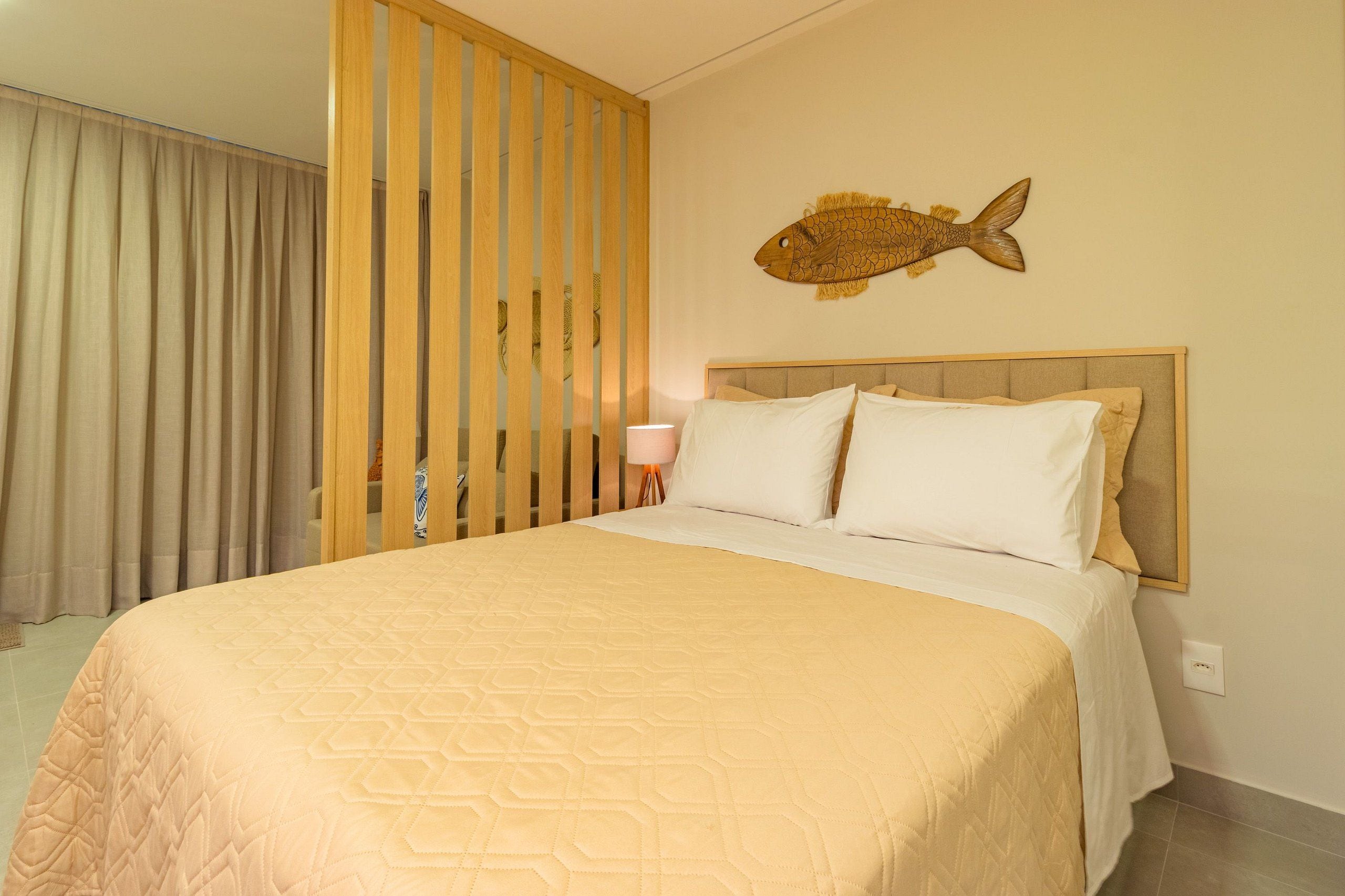 Habitación de hotel con cama, cortinas, panel de madera, decoración de pez montada en la pared y lámpara de noche.