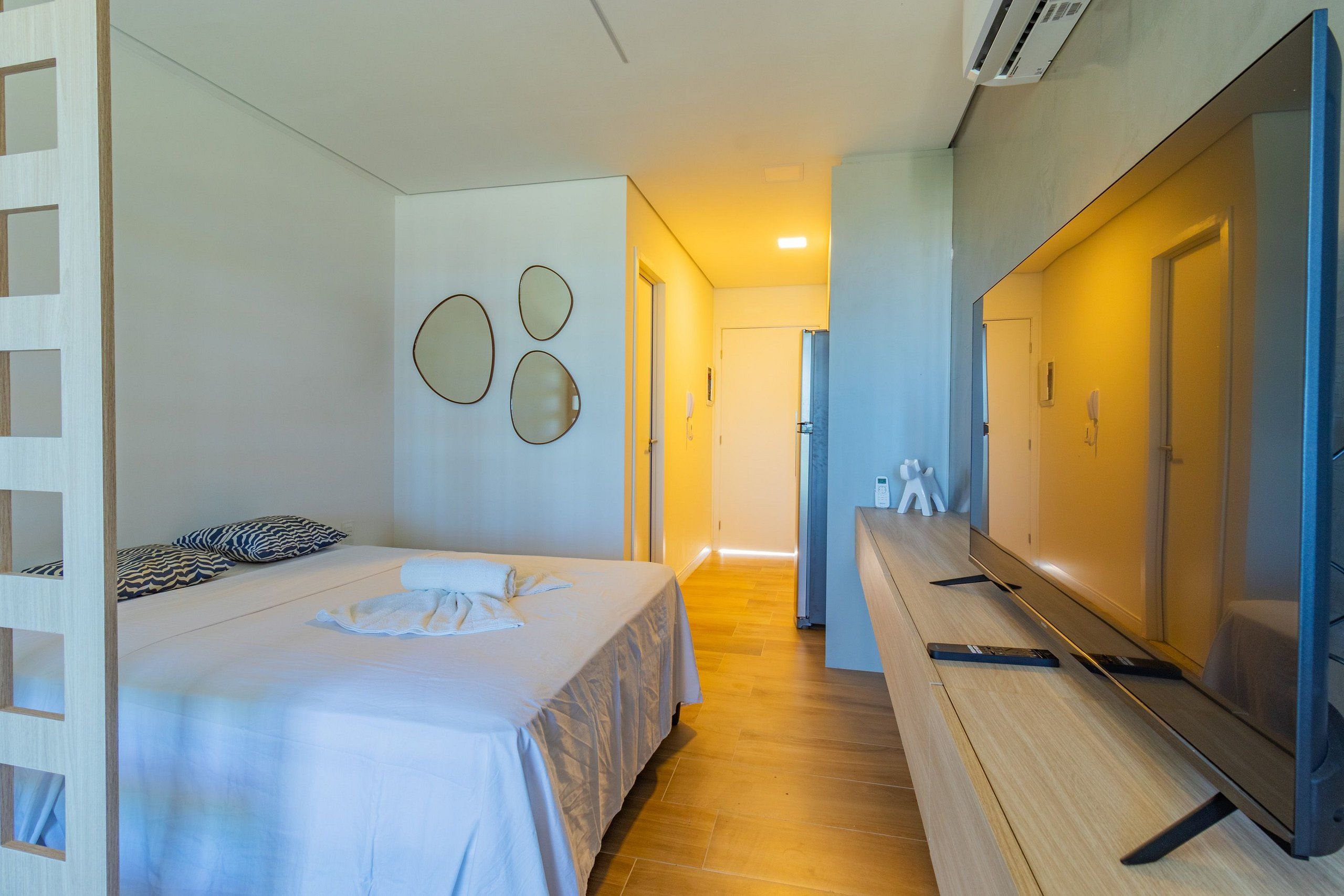 A hotel room with a bed, a TV, a desk, and a mirror on the wall.
