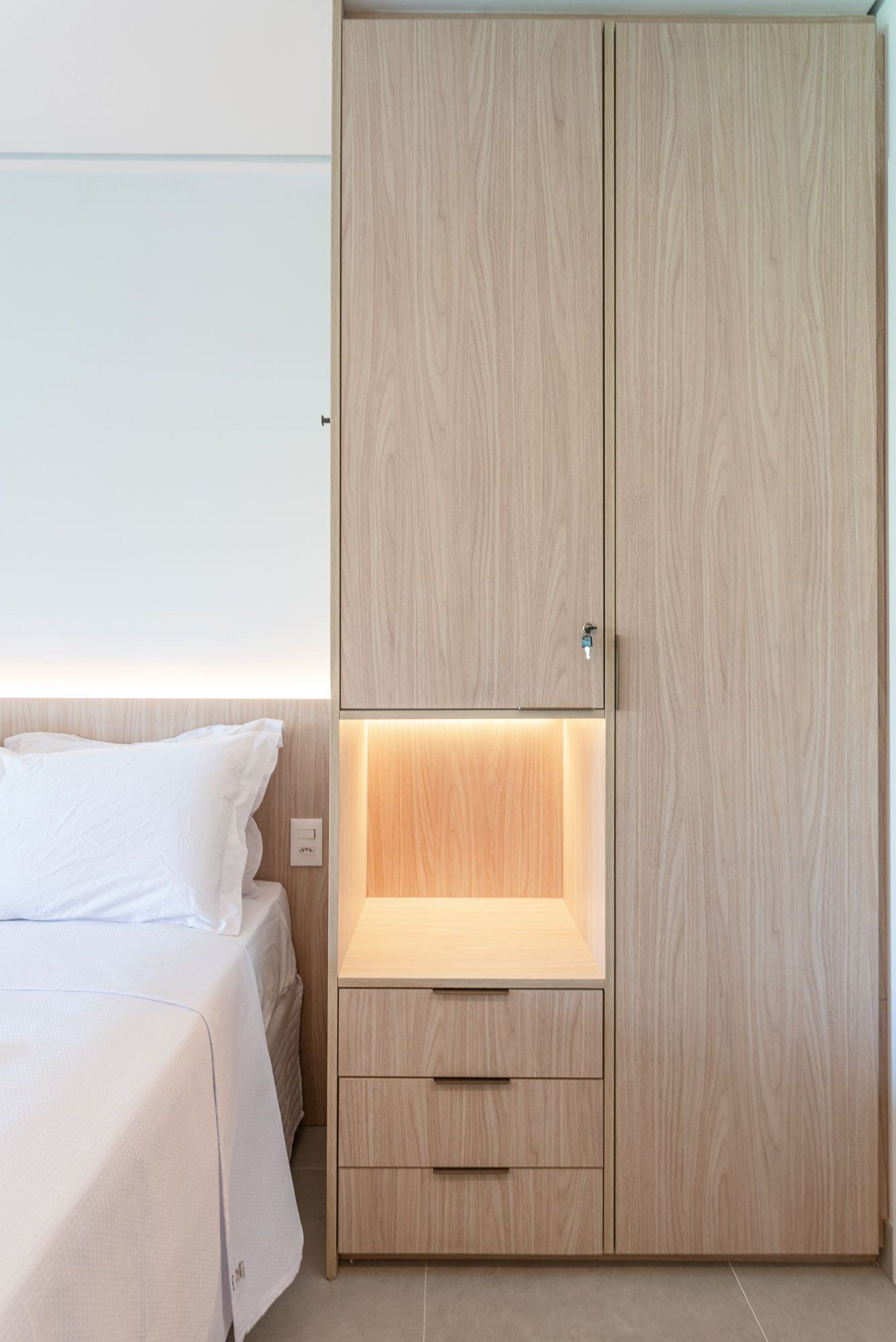 Quarto com cama, guarda-roupa de madeira com prateleira inferior e mesa de cabeceira.