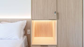Quarto com cama, guarda-roupa de madeira com prateleira inferior e mesa de cabeceira.