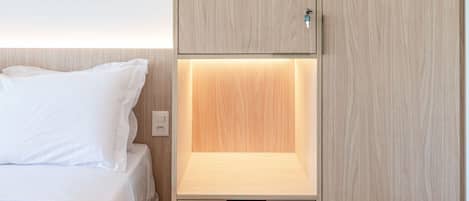 Quarto com cama, guarda-roupa de madeira com prateleira inferior e mesa de cabeceira.