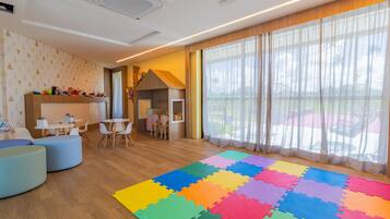 A modern room with a wooden floor, colorful foam puzzle mats, a white ceiling, and a large window with sheer curtains.