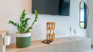 A modern living room with a wooden cabinet, a green plant in a woven basket, a framed artwork, and a mounted television.