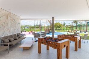 Un grand espace intérieur comprenant une table de baby-foot, un canapé et un coin jeux, le tout visible à travers de grandes fenêtres.
