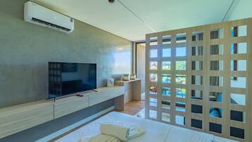 Quarto de hotel moderno com televisão de tela plana, divisória de madeira com várias janelas, cama com toalhas dobradas e ar-condicionado no teto.