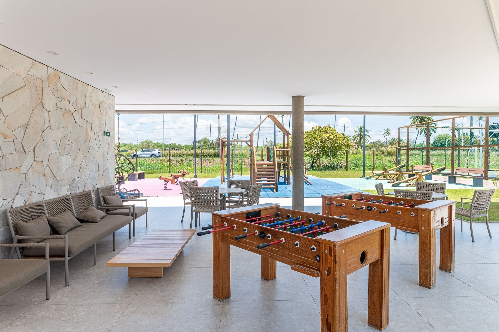 Amplo espaço interno com mesa de pebolim, sofá e área de recreação visíveis por grandes janelas.