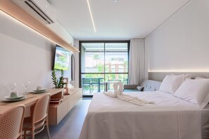 Hotellihuone, jossa on sänky, työpöytä tuoleineen, televisio ja parveke, jolta on näkymä.