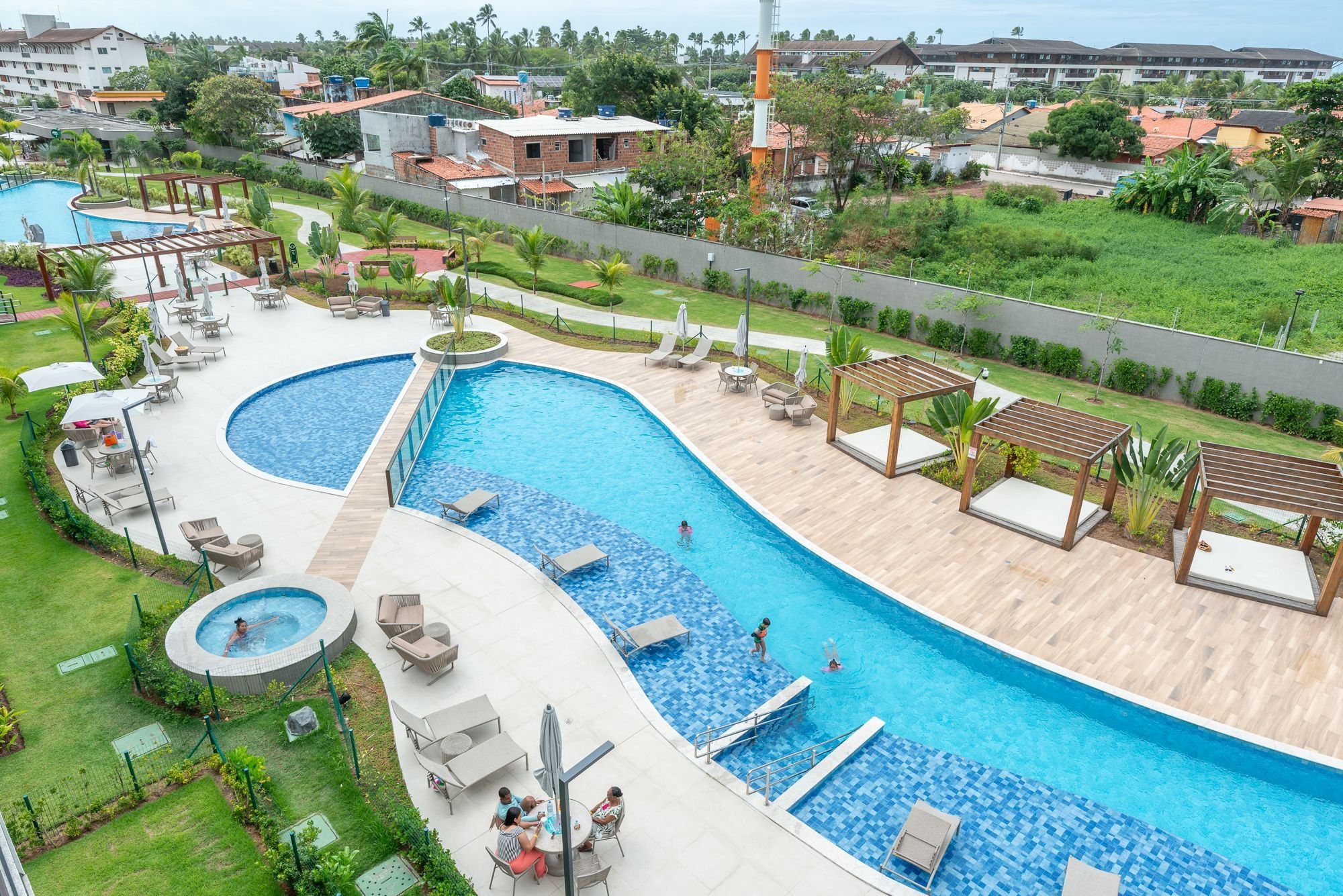 Ein großer Pool mit mehreren Sitzbereichen und einer Whirlpool-Anlage, umgeben von Grünflächen und Wohnhäusern.