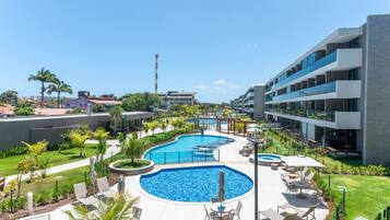 Un resort con una amplia piscina central, mobiliario exterior y un edificio moderno con balcones.