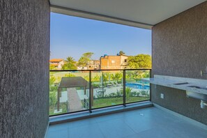 A balcony with a view of a swimming pool and greenery, a modern kitchen area, and a tiled floor. - Beach Class Summer by Carpediem (Ipojuca)