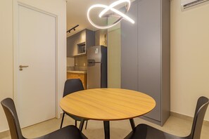 A room with a round wooden table, black chairs, a white door, a kitchen area with a refrigerator and microwave, and a grey wardrobe. - Beach Class Summer by Carpediem (Ipojuca)