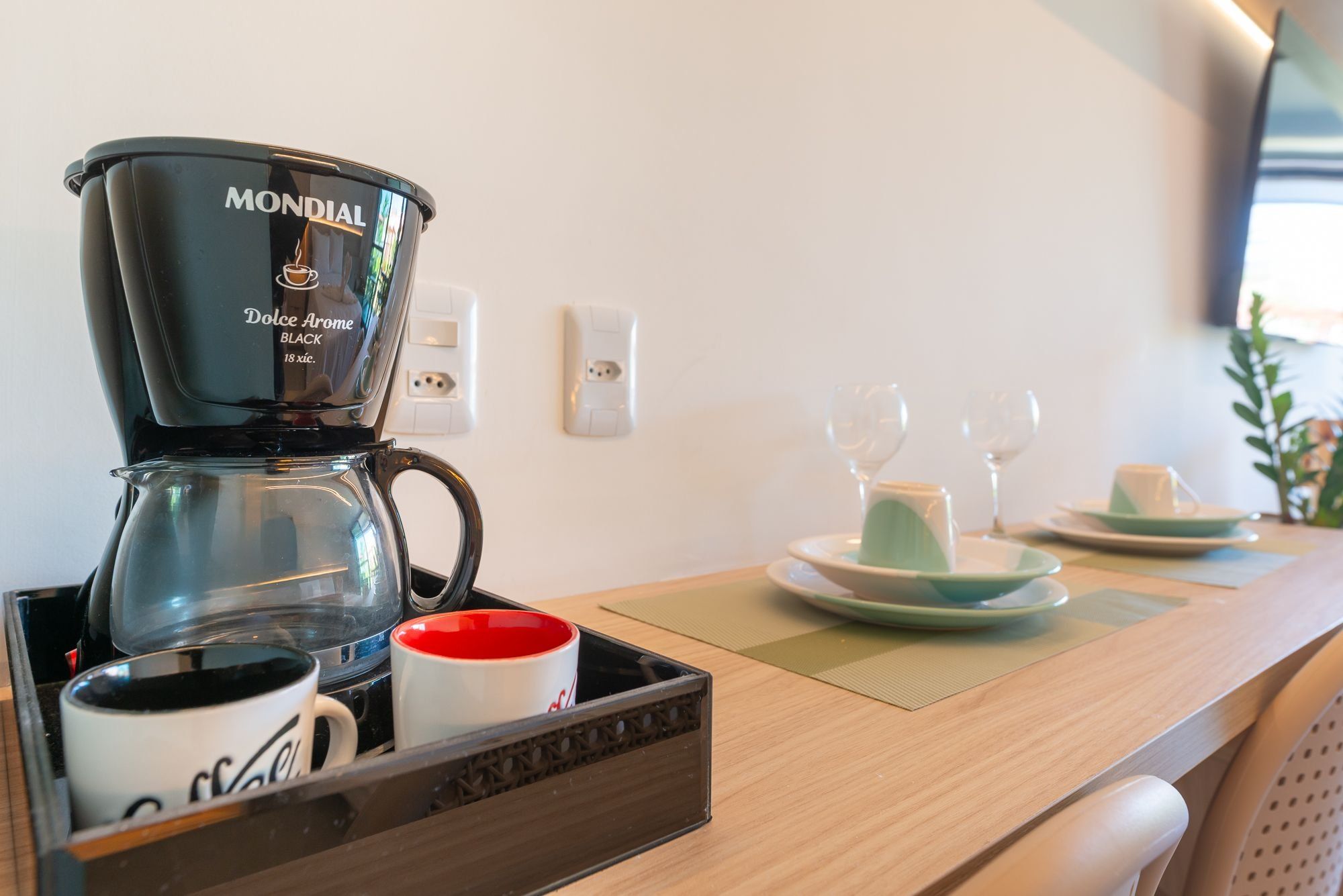 A coffee maker, a tray with mugs, and a table with plates and glasses.