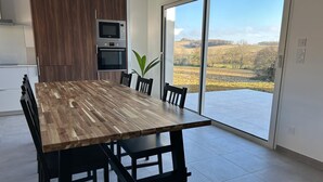 A modern kitchen with a large dining table, built-in appliances, and a view of a rural landscape through large sliding glass doors.