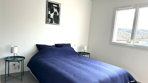 A bedroom with a large bed, two bedside tables, a window, and a wall-mounted picture.