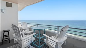 Un balcone con poltrone Adirondack bianche, un tavolino rotondo e vista sull'oceano.