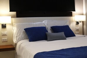 A hotel room with a bed, white bedding, blue and gray pillows, a flat-screen TV mounted on the wall, and bedside lamps. - 1BRM Infinity Homes Punta Cana (Punta Cana)