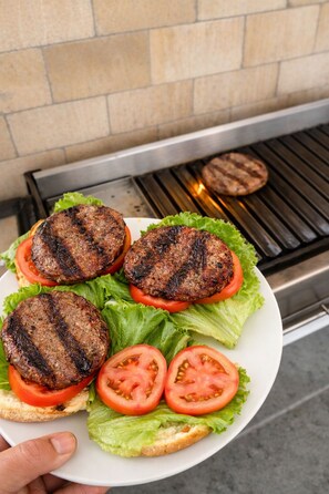 Une assiette contenant quatre hamburgers grillés, de la laitue et des tranches de tomates, placée devant un gril.