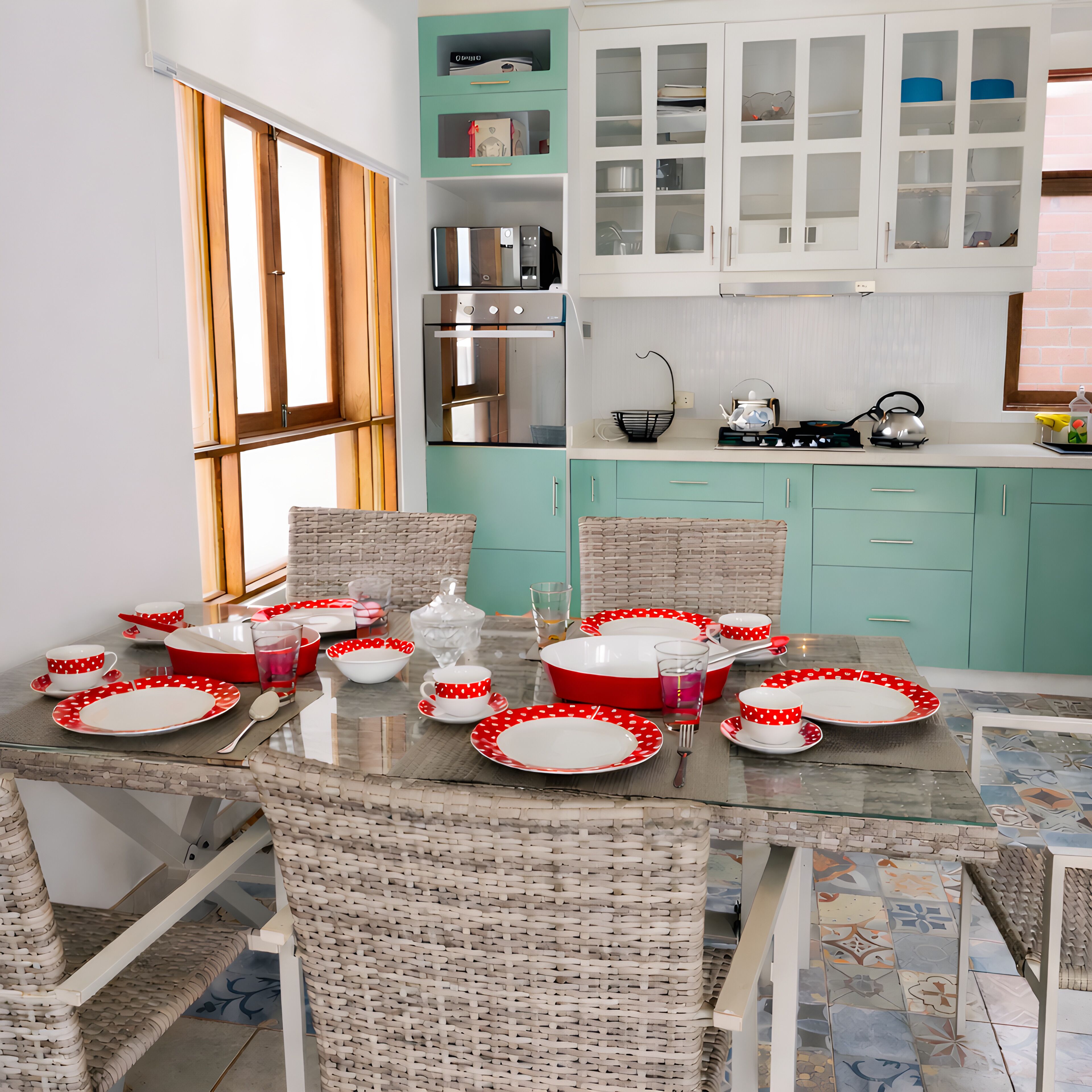Een moderne keuken met een eethoek, met een glazen tafel, rieten stoelen en kastjes in blauwgroen.