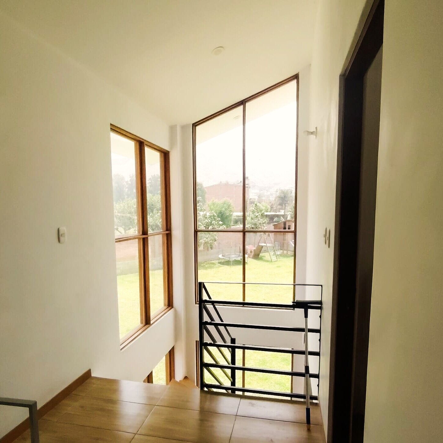Una habitación con vistas a un área verde y un edificio distante, todo visible a través de amplios ventanales.