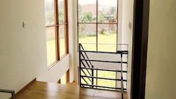 Una habitación con vistas a un área verde y un edificio distante, todo visible a través de amplios ventanales.