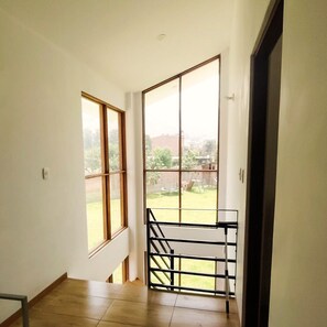 Ein Zimmer mit Blick auf eine Wiese und ein Gebäude in der Ferne, durch große Fenster.