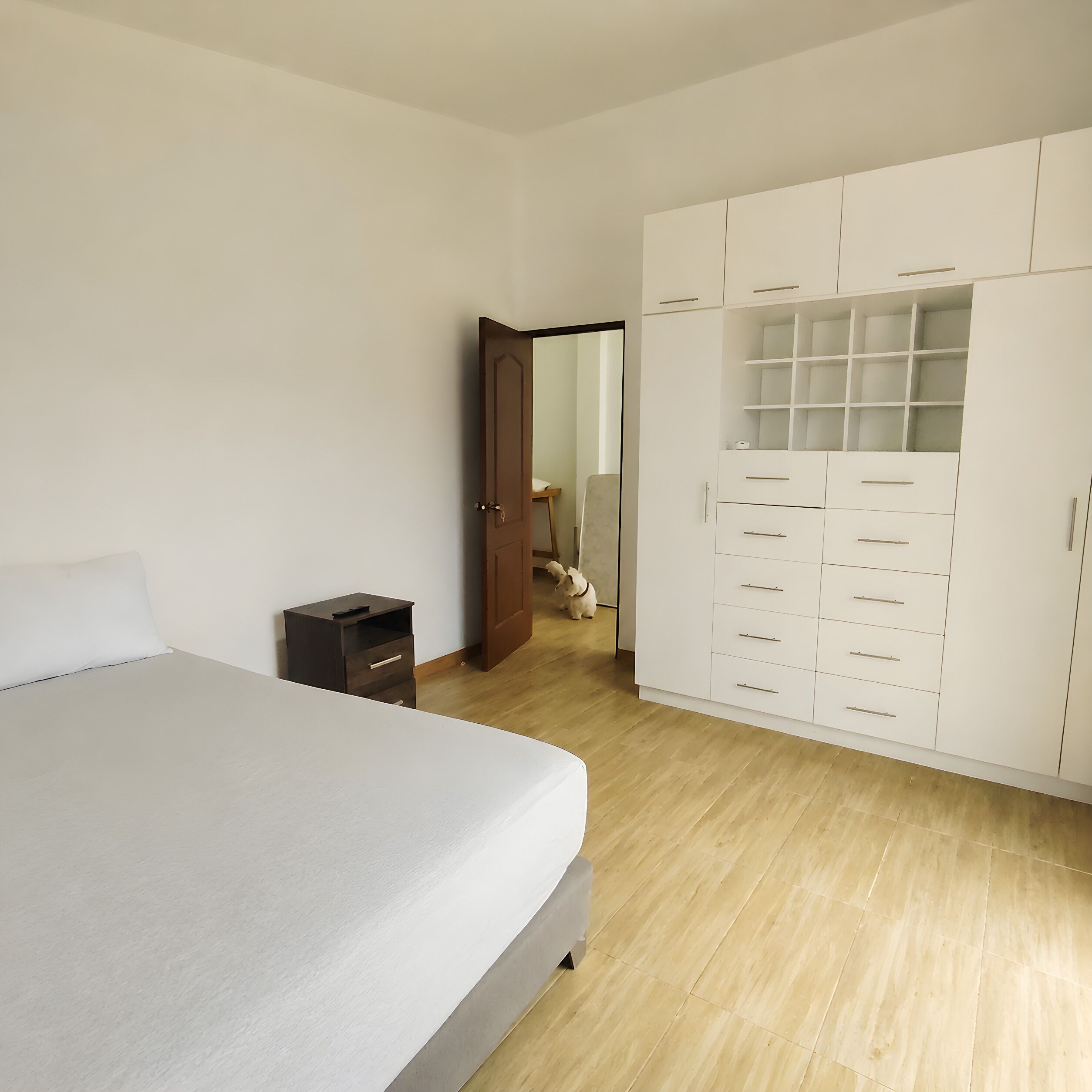 Un dormitorio con cama, armario, mesita de noche pequeña y puerta que da a otra habitación.