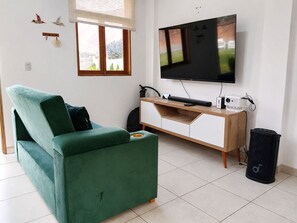 Ein Wohnzimmer mit grünem Sofa, einem flachbildfernseher an der Wand, einer Holzunterhaltungseinheit und einem Lautsprecher.