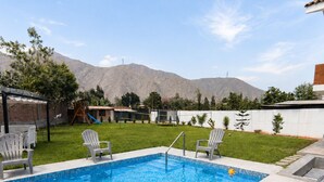 Una piscina con sillas de descanso, un parque infantil de madera y montañas al fondo.