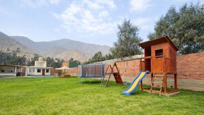 Un patio trasero con una casita de juegos de madera, un tobogán y una cama elástica.