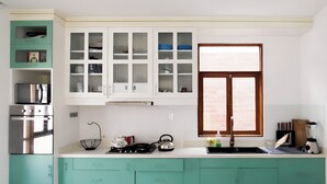 Una cocina con armarios color turquesa, estufa, lavamanos y ventana con persianas.