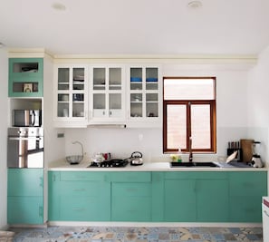 A kitchen with teal cabinets, a stove, a sink, and a window with blinds.