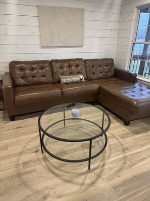 A brown leather sectional sofa with a cushion labeled "Huntsville" and a glass coffee table with metal legs.